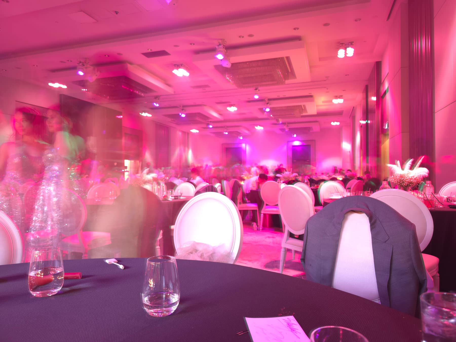 A banquet hall under magenta lighting, the people in it smeared by a long exposure.